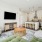 Bright sunlit living room with couch, chair, entertainment center with tv, and view of kitchen island, barstools, and stainless steel appliances 